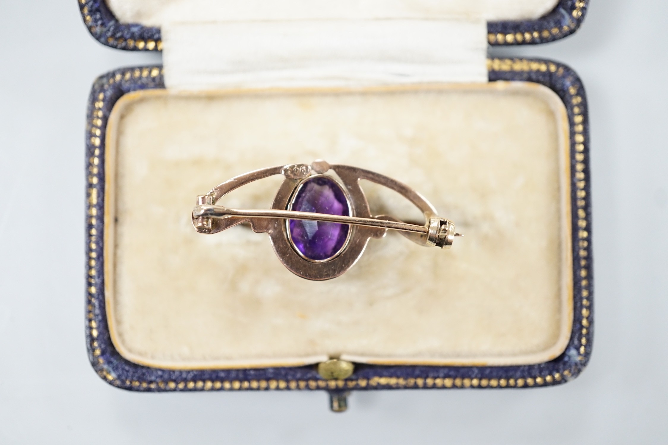 An Edwardian Art Nouveau 9ct and single stone oval cut amethyst set brooch, 31mm, gross weight 2.2 grams, in fitted gilt tooled leather box.